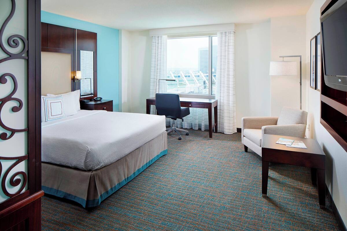A hotel room with a large bed, a desk, a chair, and a TV.