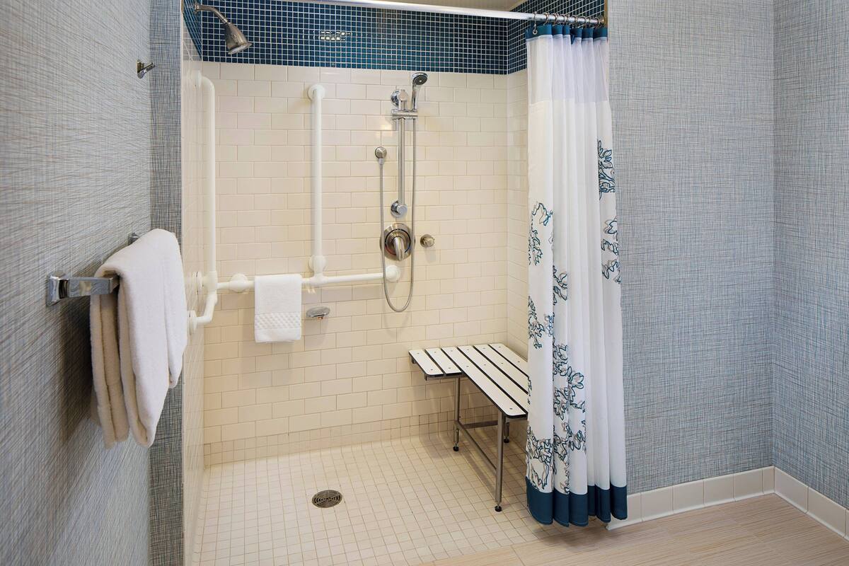 A shower area with a bench, a towel rack, and a showerhead.