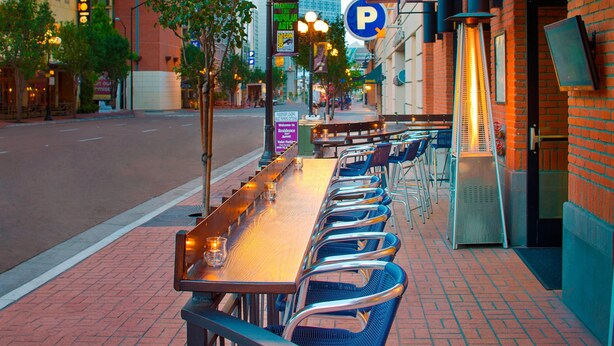 An outdoor dining area with a long table and chairs, a street view, and a building with a 'P' parking sign.