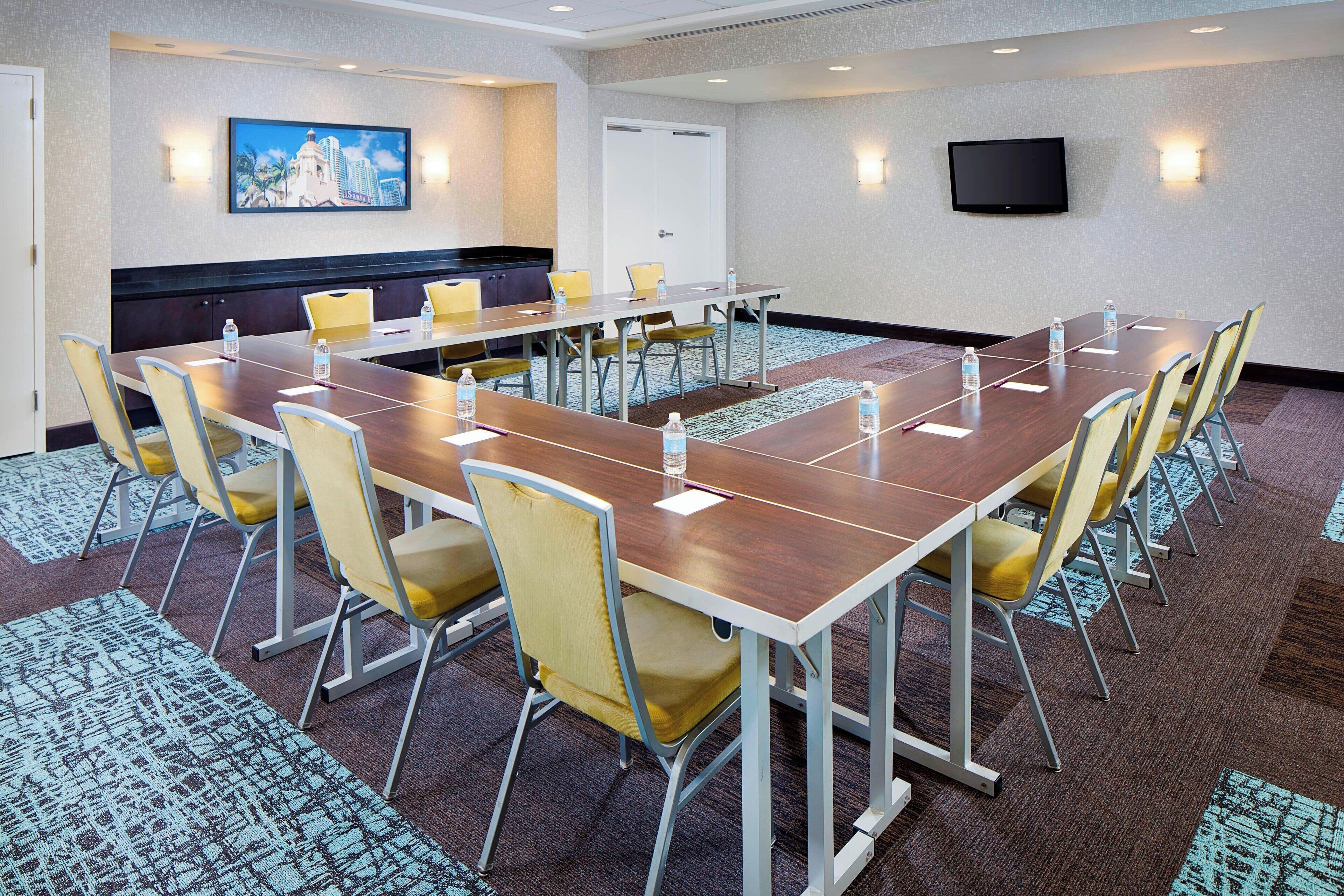 A conference room with a long table, yellow chairs, and a television mounted on the wall.
