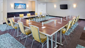 A conference room with a long table, yellow chairs, and a television mounted on the wall.