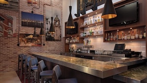 A bar area with a long counter, multiple stools, and a variety of bottles and glasses on shelves.
