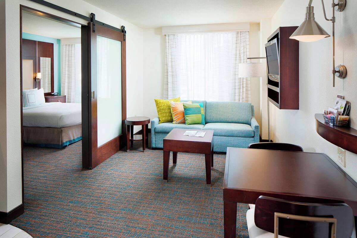 A hotel room with a bed, a sofa, a coffee table, a TV, and a lamp.
