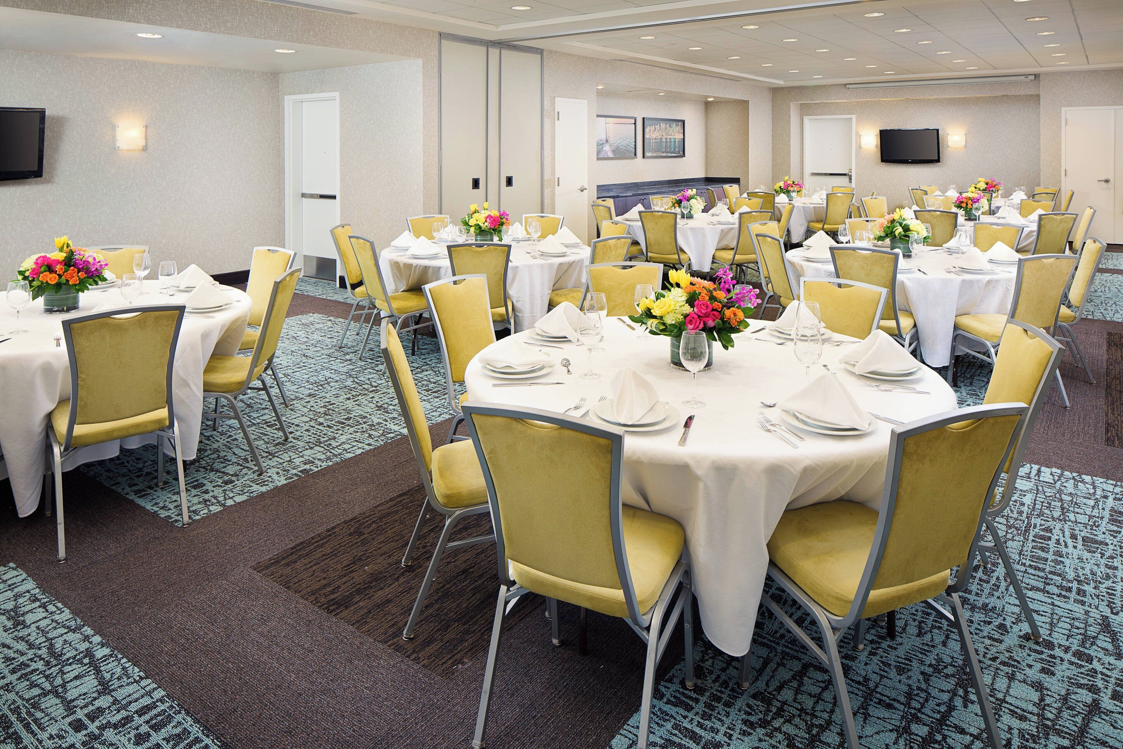 A conference room with multiple round tables, yellow chairs, and white tablecloths.