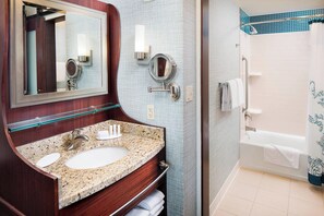 Un baño con lavamanos de granito, dos espejos, una bañera y una cortina de ducha con diseño de hojas.