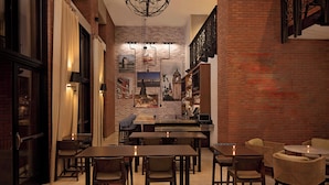 A cozy restaurant with brick walls, wooden tables, and chairs. There are candles on the tables, and a chandelier hangs from the ceiling.