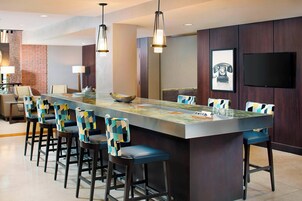 A modern bar area with a long counter, multiple bar stools, pendant lighting, and a flat-screen TV mounted on the wall.