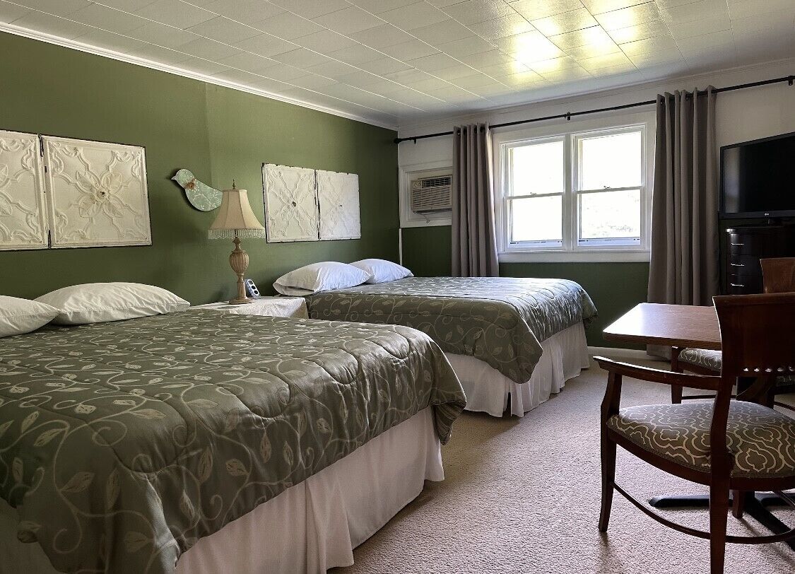 A hotel room with two beds, a desk, a chair, a television, and artwork on the walls.