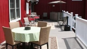 An outdoor patio with a round table and chairs, a white railing, and a red building in the background. - The Barron Brook Inn (Whitefield)