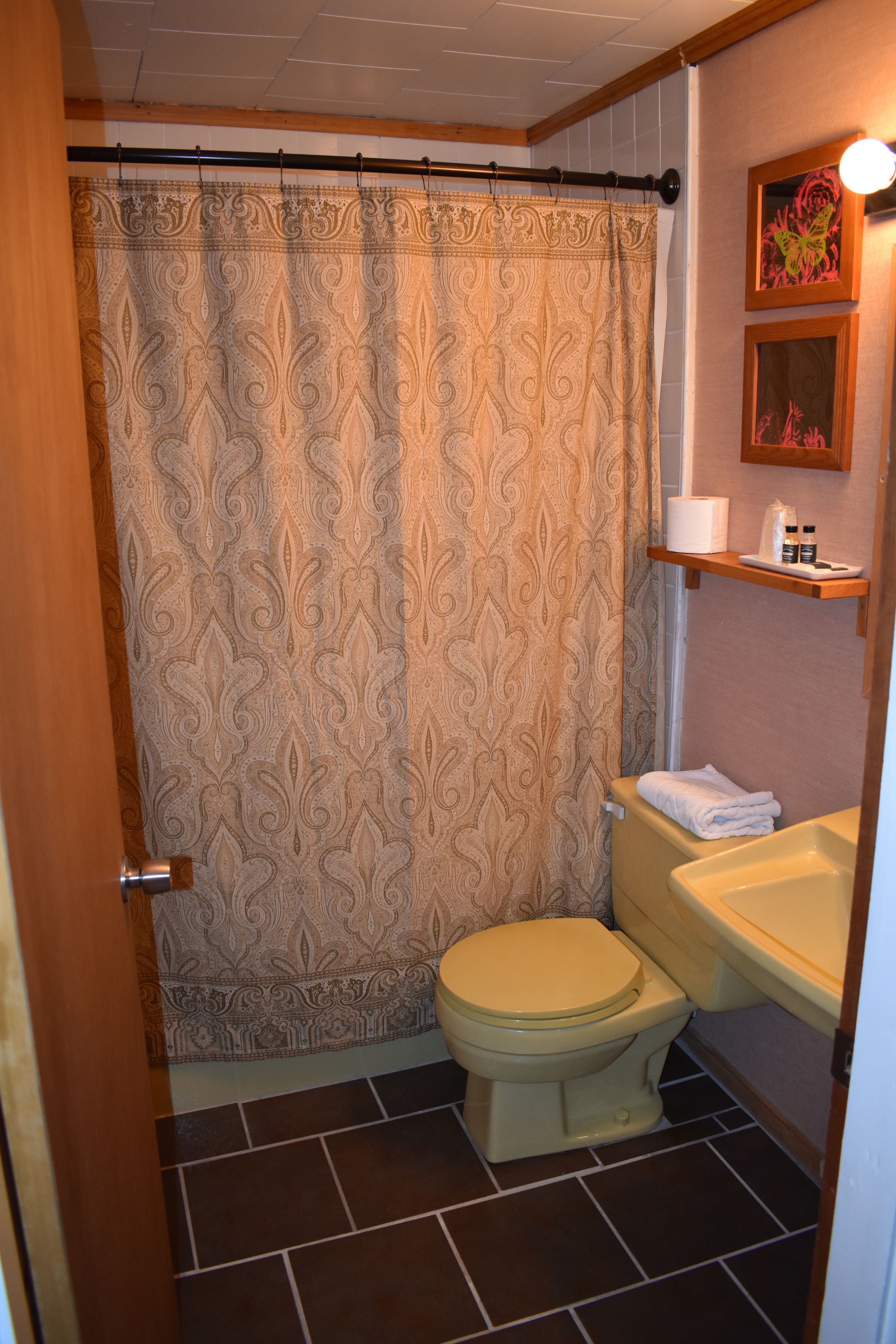 A bathroom with a patterned shower curtain, a toilet, and a sink with a shelf above it.