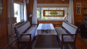 A dining area with a table and benches, a ceiling fan, a window with curtains, and a stained glass window. - The Barron Brook Inn (Whitefield)