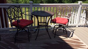 A covered outdoor patio with two metal chairs and a small round table, surrounded by a white railing.