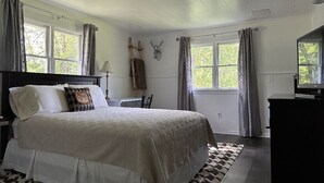 A bedroom with a large bed, two windows with curtains, a wooden chair, a desk, and a mirror. - The Barron Brook Inn (Whitefield)