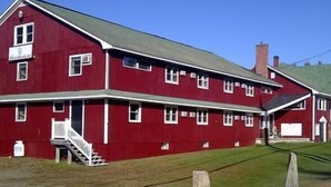 A red two-story building with a green roof, a front porch, and a staircase leading to the entrance.