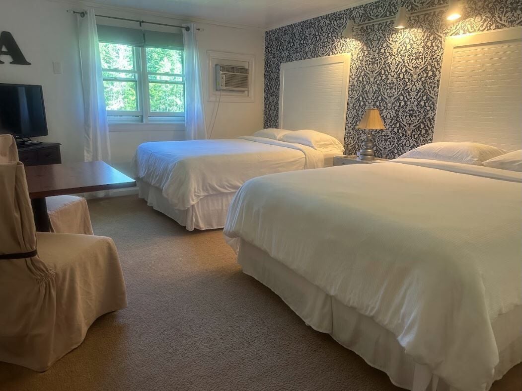 A hotel room with two single beds, a desk with a chair, a television, and a window with curtains.