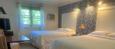 A hotel room with two single beds, a desk with a chair, a television, and a window with curtains.