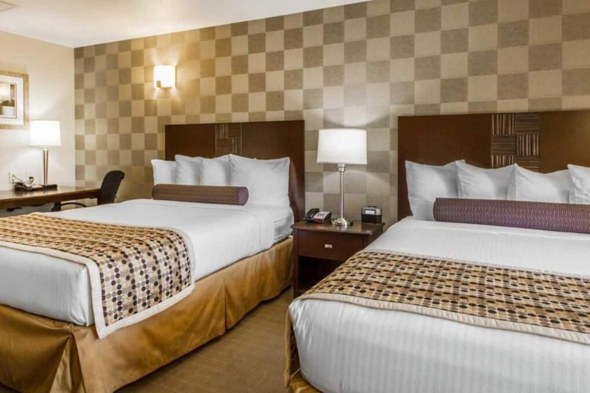 Une chambre d’hôtel avec deux lits, un bureau, une chaise et une lampe fixée au mur.