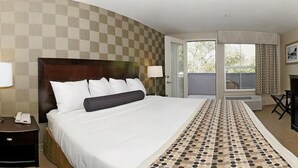 A hotel room with a large bed, a bedside table with a lamp, a chair, and a view of the outdoors through a door. - Hotel Med Park, an Ascend Collection Hotel (Sacramento)