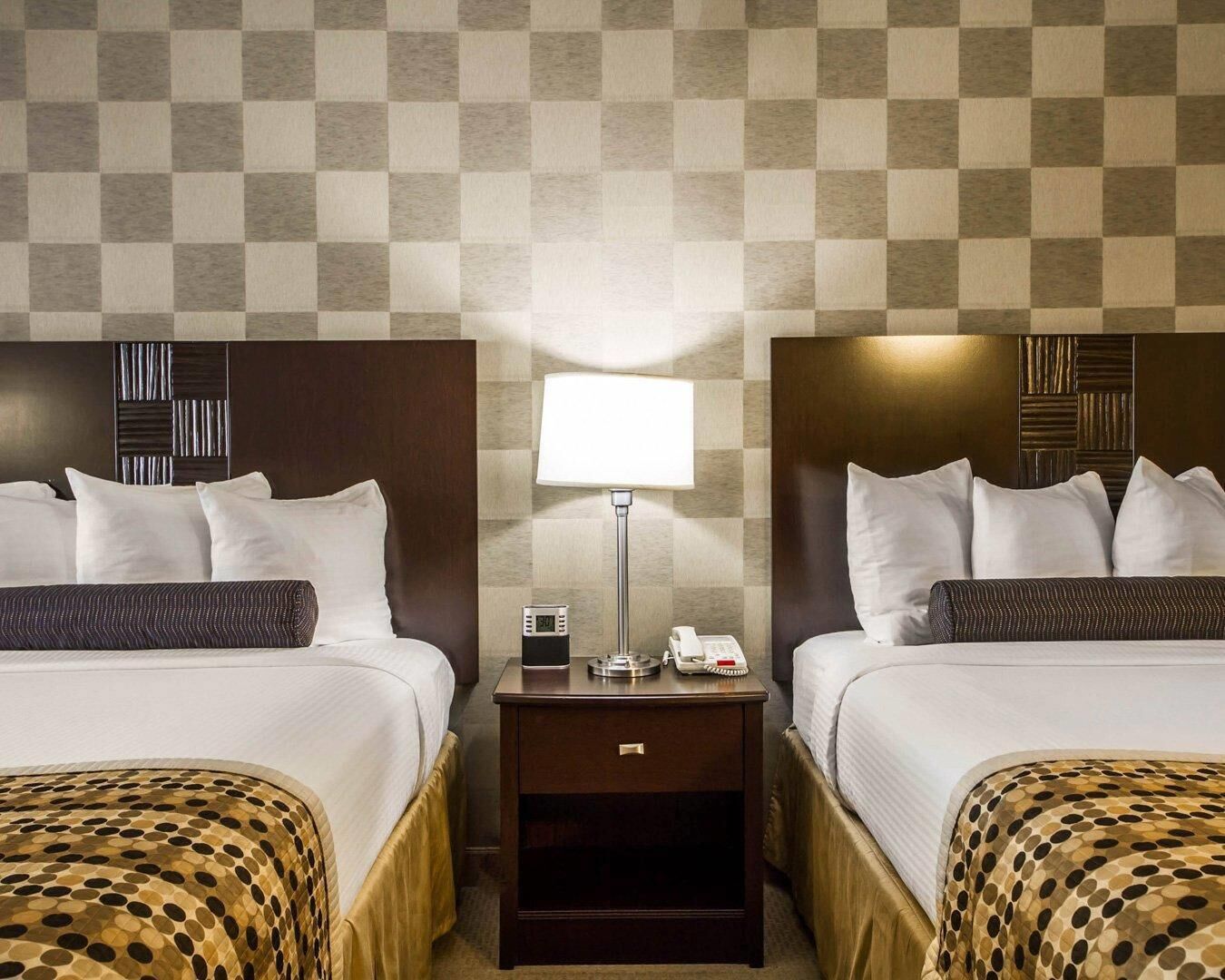 Une chambre d’hôtel avec deux lits, une table de chevet avec une lampe et une horloge numérique.