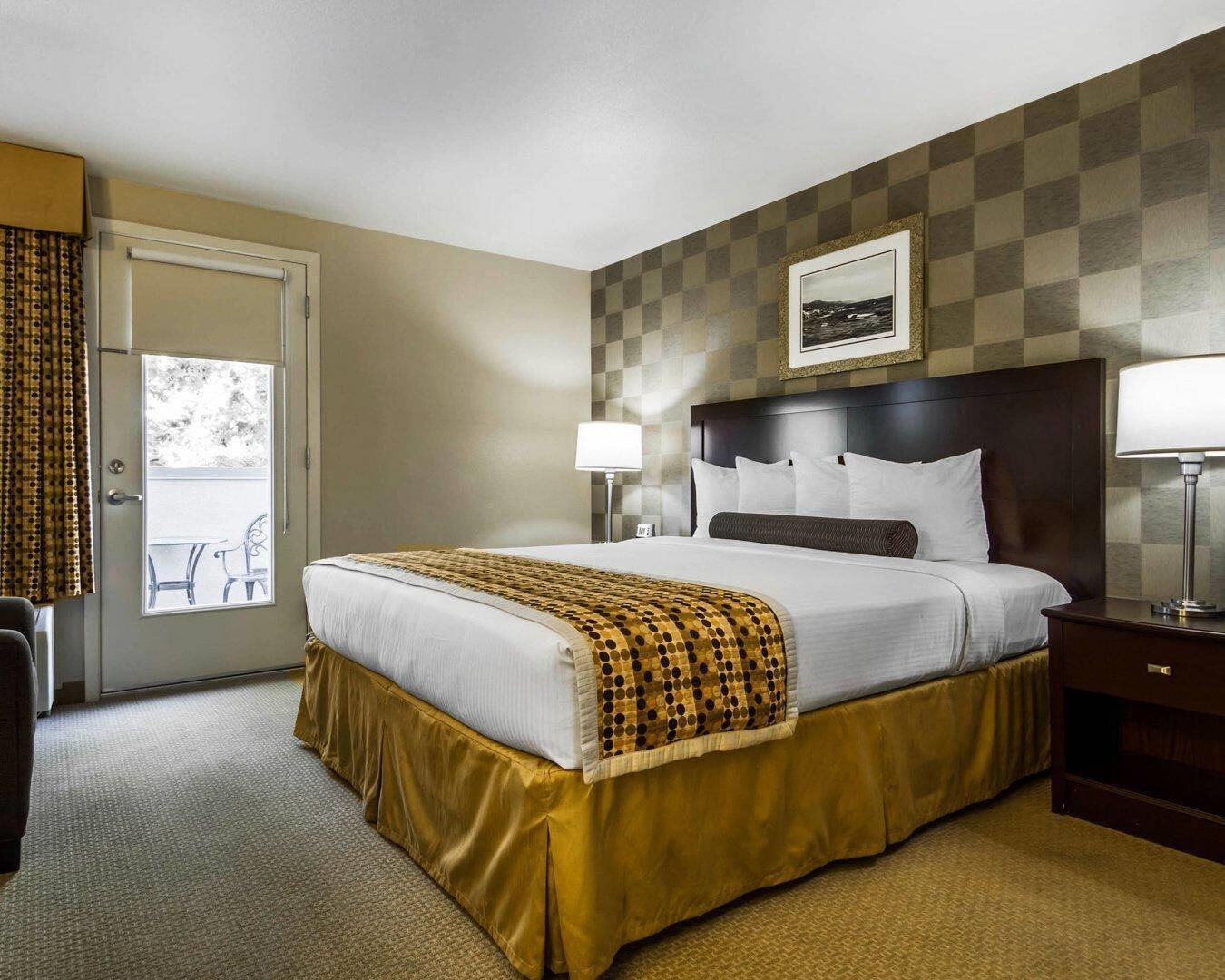 Une chambre d’hôtel avec un lit, une table de chevet, une lampe, une porte donnant sur une vue agréable et un motif à carreaux sur le mur.