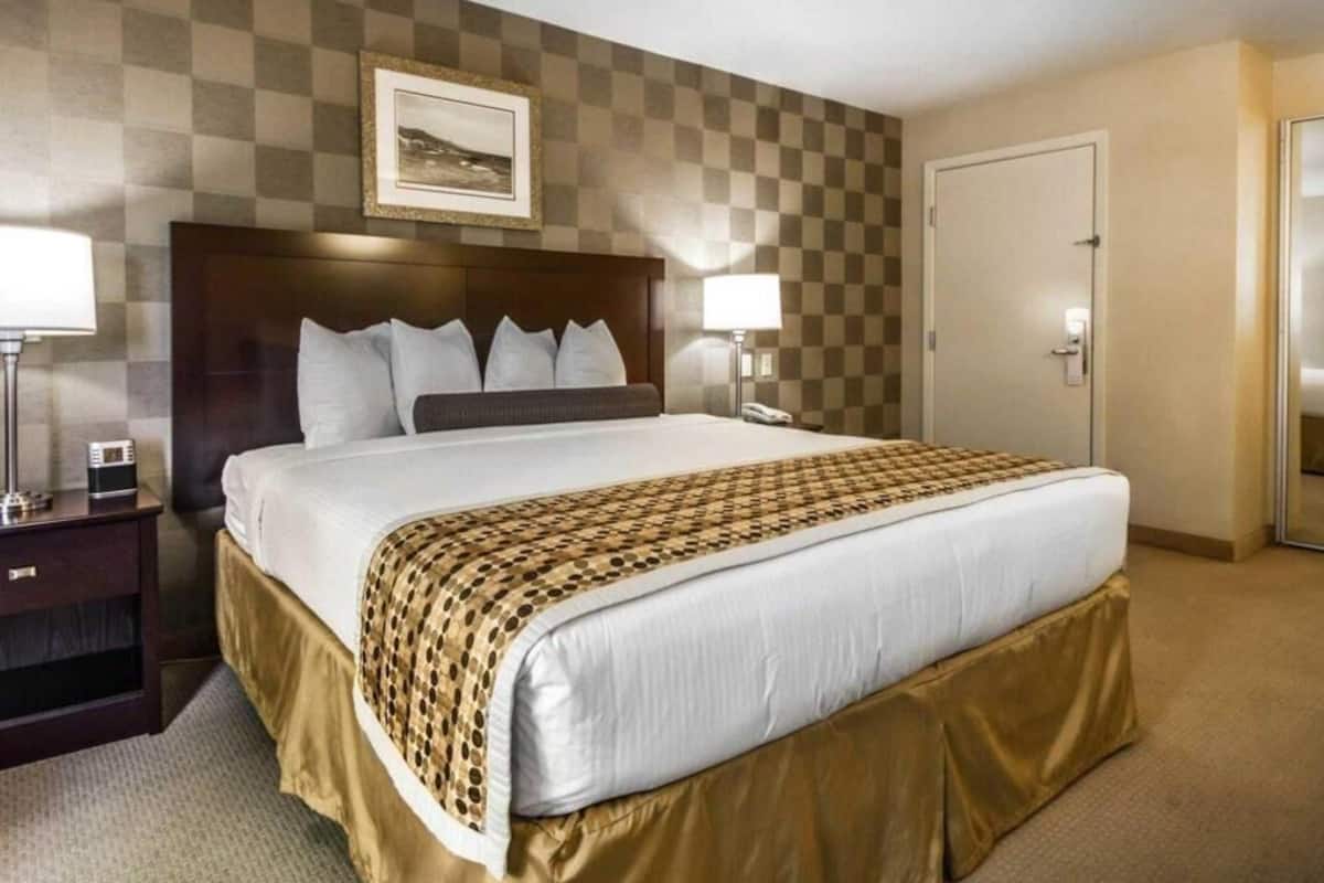 Une chambre d’hôtel avec un grand lit, deux tables de chevet, une tête de lit et un mur à carreaux, ainsi qu’une porte.