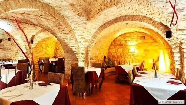 Un interior con arcos de piedra, mesas dispuestas para comer y sillas de mimbre.
