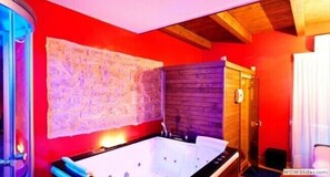 A bathroom with a large bathtub, a wooden wall panel, and a red wall.
