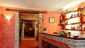 Una zona de bar con un arco de piedra que conduce a una sala, estanterías con botellas y un reloj en la pared.
