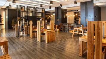 Interior moderno de restaurante con mesas y sillas de madera, zona de bar e iluminación colgante.