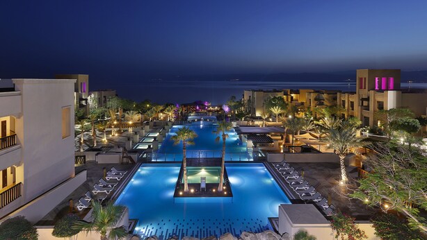 A pool area with lounge chairs and a view of the ocean at night.