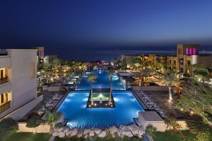 A pool area with lounge chairs and a view of the ocean at night. - Holiday Inn Resort Dead Sea by IHG (Sweimeh)