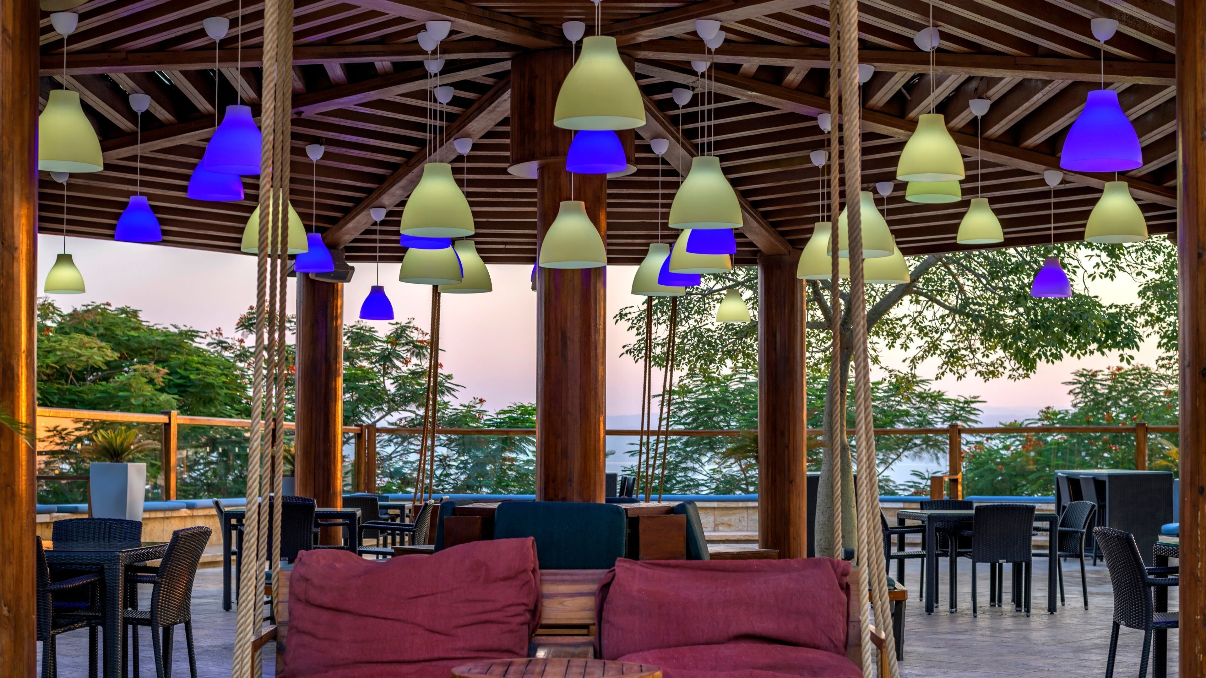 An outdoor seating area with a wooden pergola, hanging pendant lights, and a view of the sea.