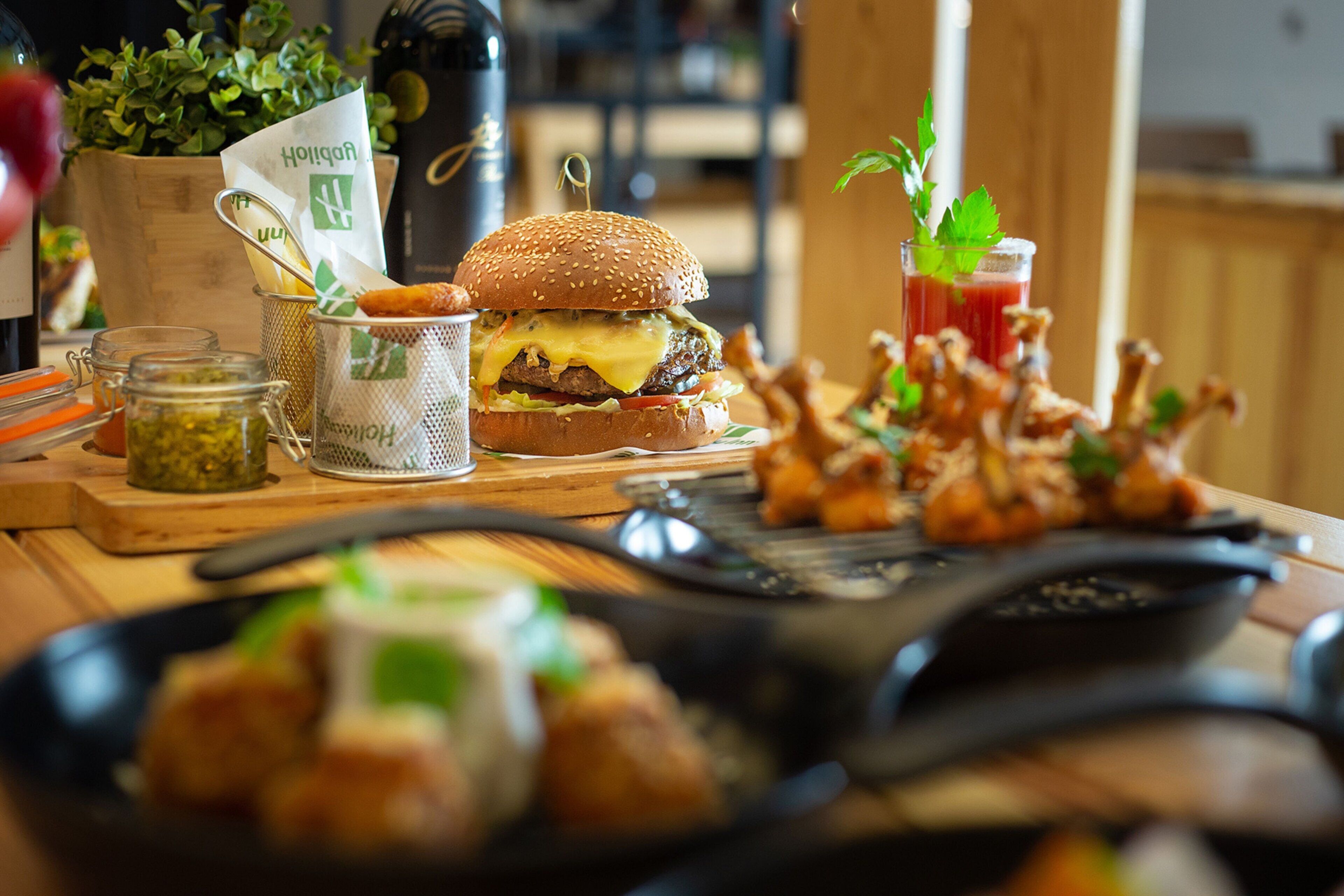 Une table à manger avec un hamburger, des frites, une boisson et des condiments.