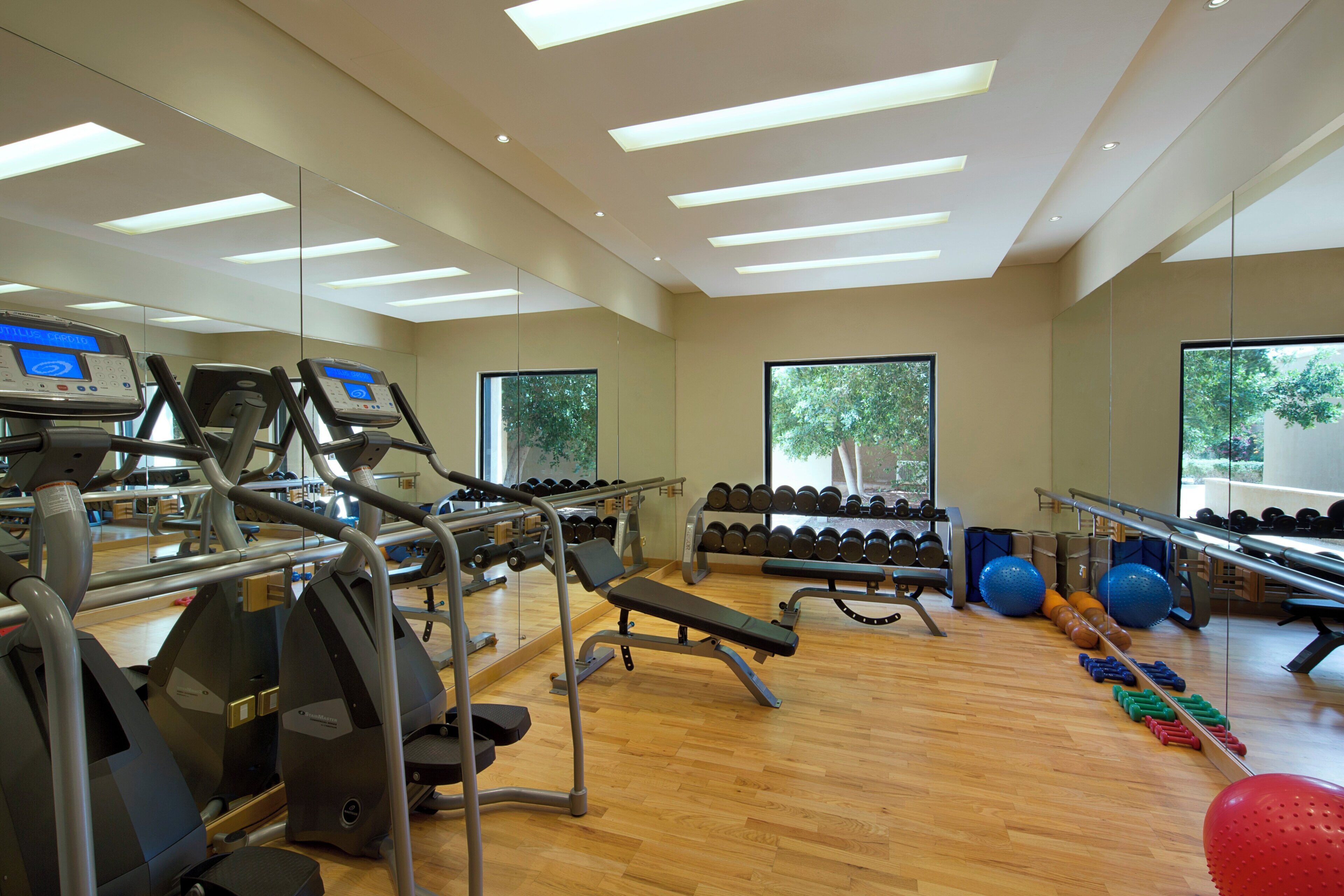 A gym with exercise equipment, mirrors, and large windows.