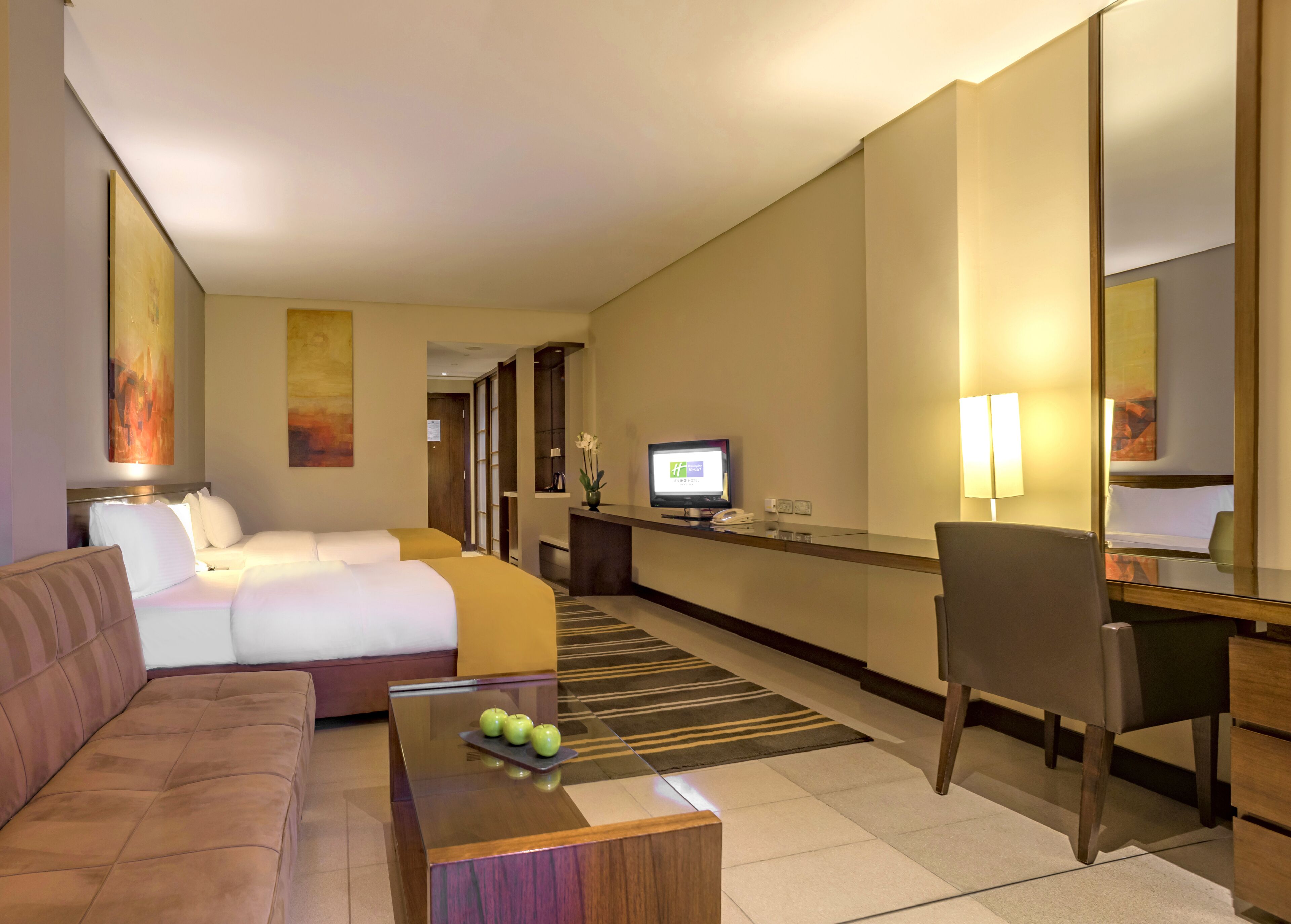 Une chambre d’hôtel comprenant un lit, un canapé, un bureau avec un ordinateur, une chaise, une télévision et un miroir.