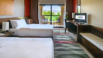 A hotel room with two beds, a desk with a computer, a TV, and a view of the outdoors.
