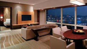 A modern hotel room with a large window offering a city view, a sofa, a coffee table, and a TV mounted on the wall. - Hyatt Regency Hong Kong, Tsim Sha Tsui (Kowloon)