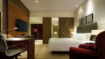 Een hotelkamer met een bed, een bureau met stoel, een televisie en een rode fauteuil.