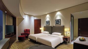 A hotel room with a large bed, a TV, a red chair, and a desk with a fruit bowl.