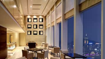 A modern hotel lobby with a city view, featuring a reception desk, seating area, and a wall with recessed lighting.