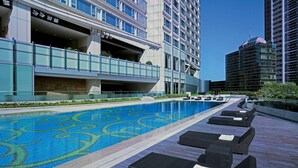 A modern hotel with a rooftop pool featuring a blue and green design, a covered parking area, and a view of surrounding high-rise buildings. - Hyatt Regency Hong Kong, Tsim Sha Tsui (Kowloon)