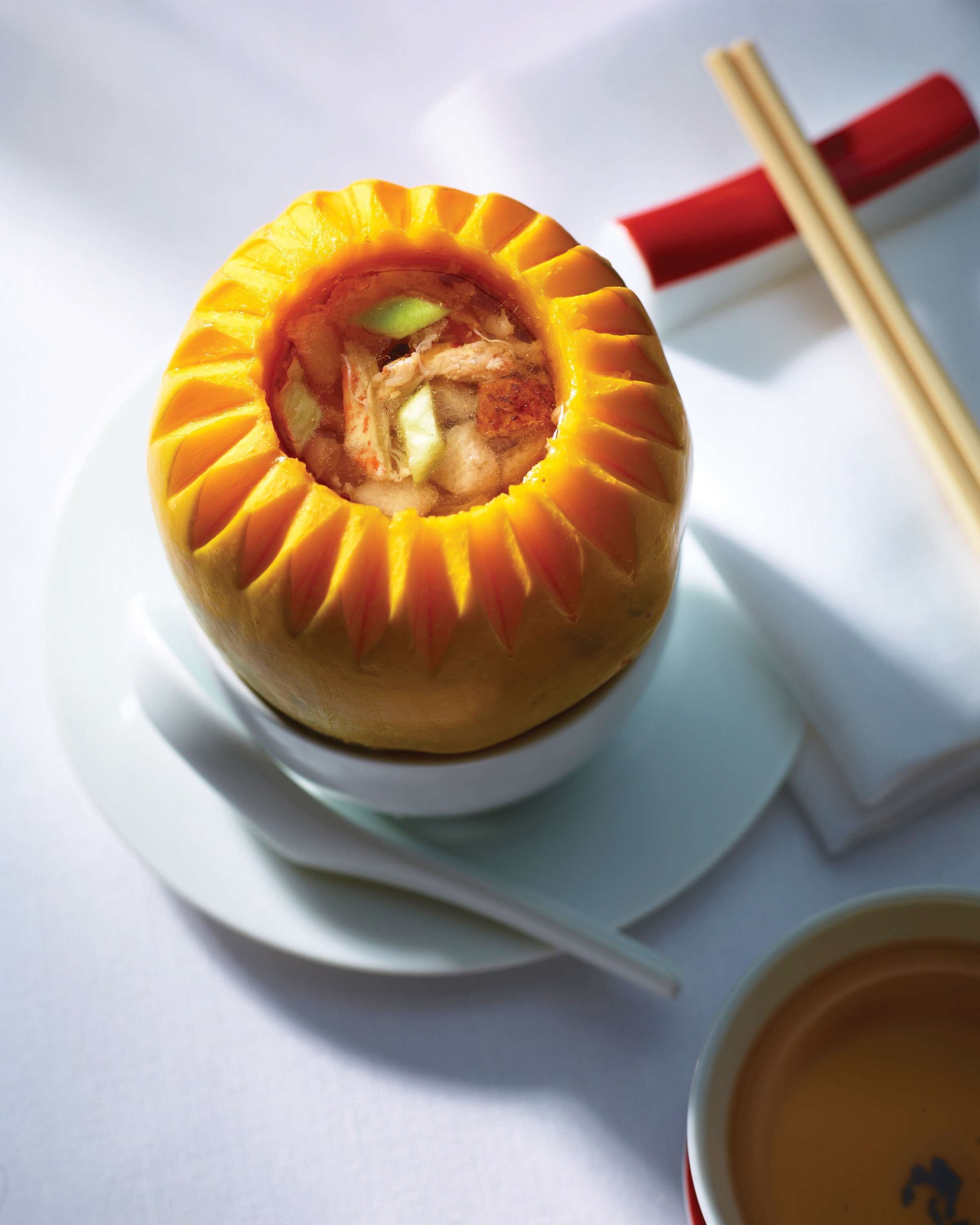 A bowl of soup with chopsticks and a napkin on a white table.