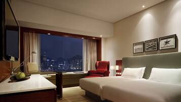 Habitación de hotel con cama, escritorio, silla, televisor y vista nocturna de la ciudad.