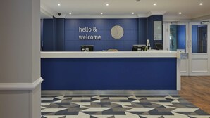 A reception desk with a blue wall and a clock. - Travelodge Bath Waterside (Bath)