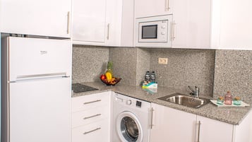 Cocina compacta con refrigerador, microondas, lavadora, pileta y encimera de granito.