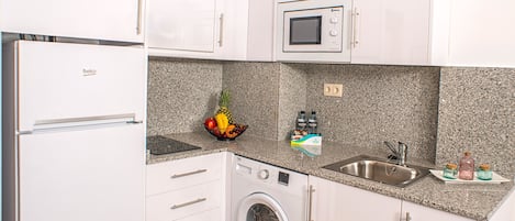 Cocina compacta con refrigerador, microondas, lavadora, pileta y encimera de granito.