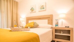 A hotel room with a bed, bedside lamps, a nightstand, a basket with breakfast items, and two wall art pieces. - Ona Suites Salou (Salou)