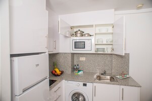 Una cocina compacta con lavadora, microondas y un lavamanos pequeño.