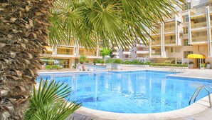 A swimming pool surrounded by a multi-story building with balconies, palm trees, and a sun umbrella. - Ona Suites Salou (Salou)