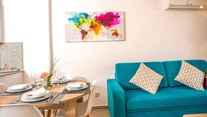 A modern living room with a teal sofa, a dining table set with plates and glasses, and a colorful abstract painting on the wall. - Ona Suites Salou (Salou)